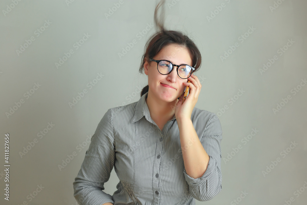 Smiling pretty brunette girl with eyeglasses calling phone and talking isolated over gray background Smiling pretty brunette girl with eyeglasses calling phone and talking isolated over gray background