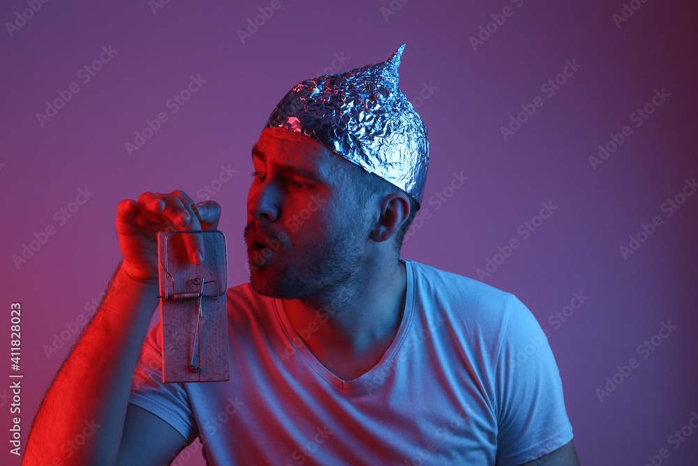 Emotional Bearded Man in foil hat is caught finger in mousetrap in red-blue neon light - obrazy, fototapety, plakaty 