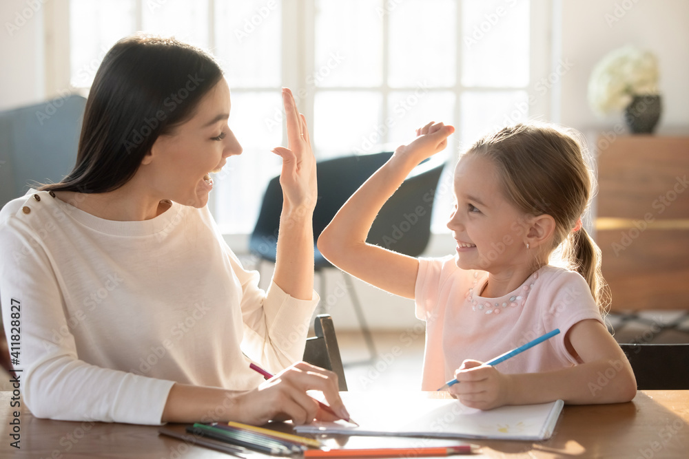 Overjoyed young Caucasian mother and small 7s daughter give high five drawing together in album. Happy mom and little girl child celebrate accomplishment involved in funny learning activity painting. Overjoyed young Caucasian mother and small 7s daughter give high five drawing together in album. Happy mom and little girl child celebrate accomplishment involved in funny learning activity painting.