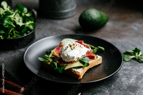 Breakfast. Sandwich with ham, poached egg, avocado and spinach in a plate on a dark background