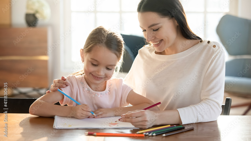 Smiling young Caucasian mother and little 7s cute daughter have fun drawing in album with pencils together. Happy mom and small girl child paint involved in funny learning activity. Hobby concept. Smiling young Caucasian mother and little 7s cute daughter have fun drawing in album with pencils together. Happy mom and small girl child paint involved in funny learning activity. Hobby concept.