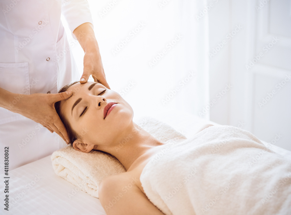 Beautiful woman enjoying facial massage with closed eyes in sunny spa center