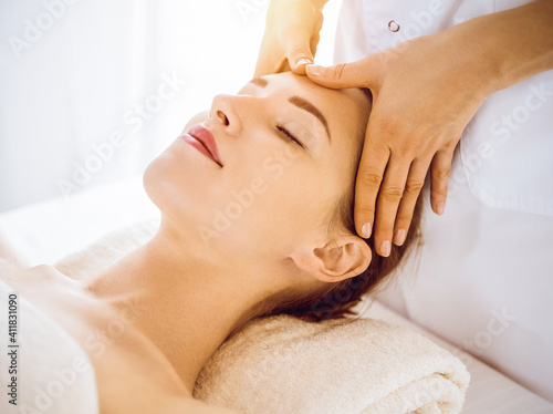 Beautiful woman enjoying facial massage with closed eyes in sunny spa center