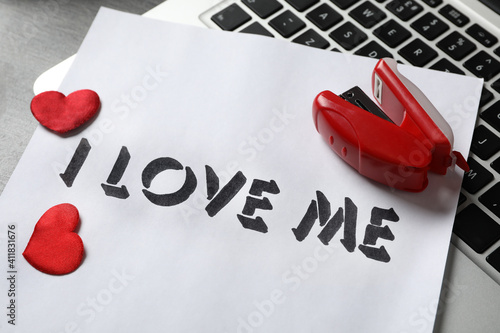 Paper with phrase I Love Me, laptop, red hearts and stapler on desk, closeup