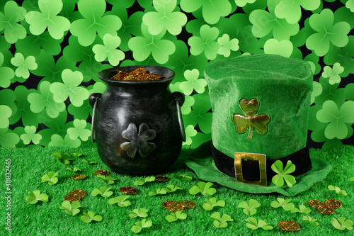 Cast iron pot with four-petal lucky shamrock leaf, full of gold coins, leprechaun hat, clover leaves and gold coins on green grass and shamrock leaves backround. Saint Patricks Day banner, poster