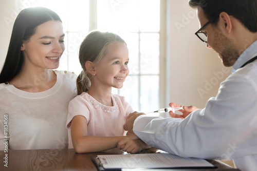 Caring male doctor give arm injection to small Caucasian girl patient at checkup in hospital. Man pediatrician prick little child with syringe, cure treat from illness. Children healthcare concept.