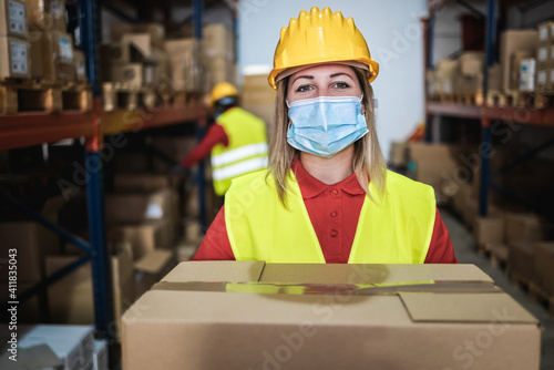 Warehouse worker woman holding delivery box while wearing safety mask for coronavirus prevention - Focus on face © DisobeyArt