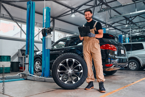 Concept of working in a car service center. Mechanic notes tire condition, tire tread, lifetime, alloy strength wheels and brake systems for safety. © HBS