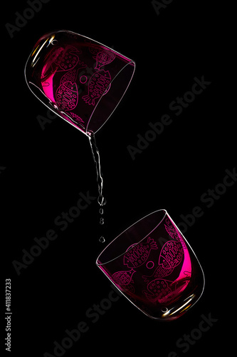 Two purple crystal glasses. One glass spills a stream of liquid over another. Dark background. backlight. Copy space. Elegant scene