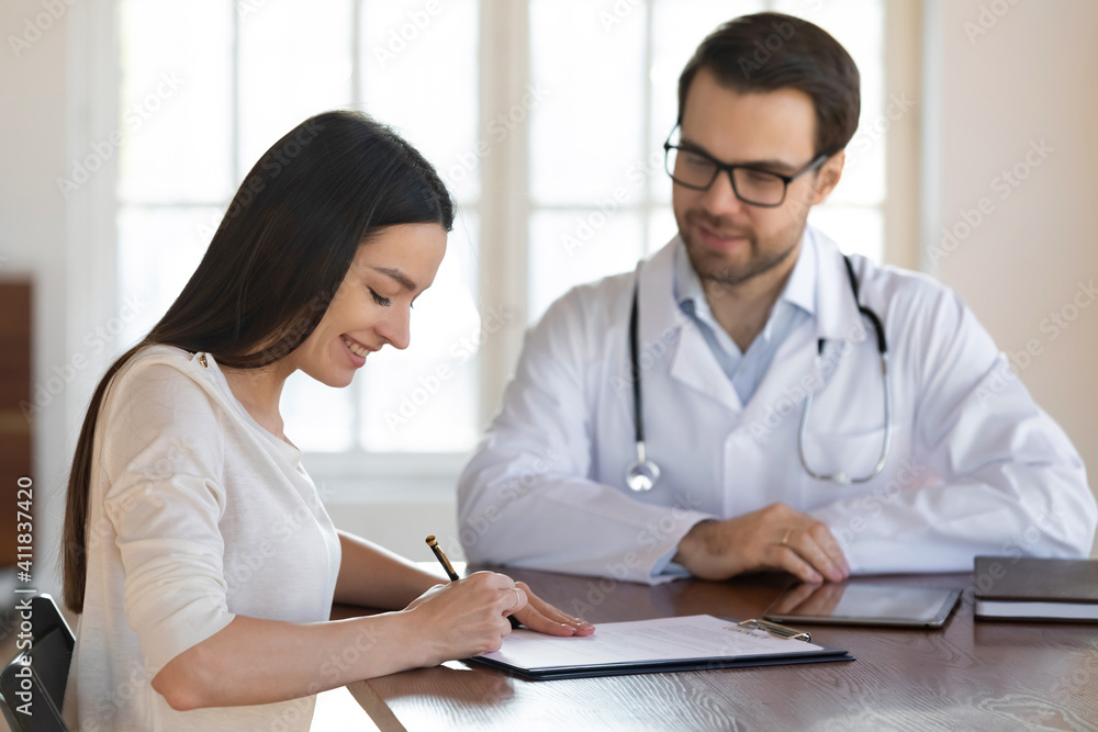 Smiling female Caucasian patient sign paper contract make health insurance agreement with male doctor in clinic. Woman client put signature on document close deal with therapist on private hospital. Smiling female Caucasian patient sign paper contract make health insurance agreement with male doctor in clinic. Woman client put signature on document close deal with therapist on private hospital.