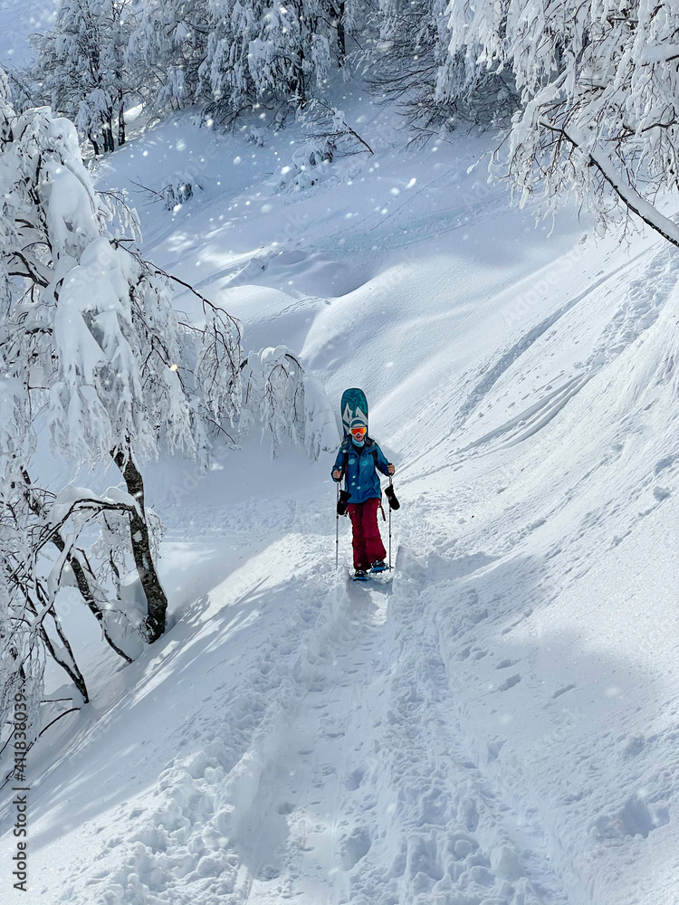 VERTICAL: Fit woman on snowboarding adventure snowshoes up a mountain trail.
