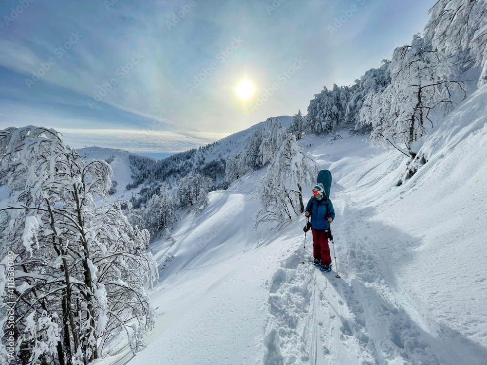VERTICAL: Female snowboarder observes the wintry landscape while snowshoeing.