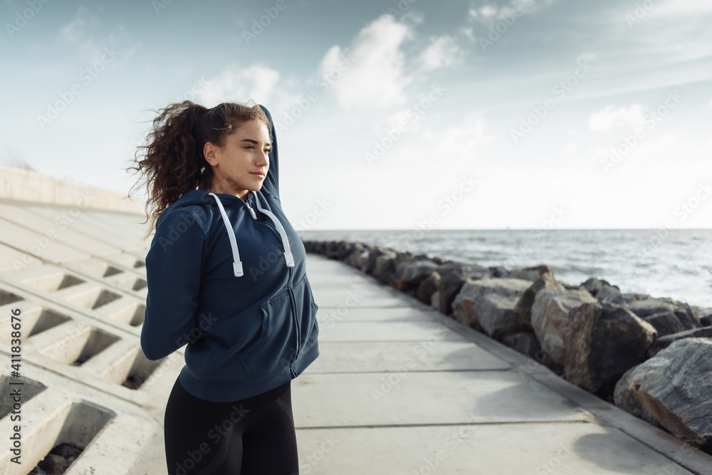 Curly sports woman in sportswear doing body warming up before training on urban beach. Healthy lifestyle Curly sports woman in sportswear doing body warming up before training on urban beach. Healthy lifestyle