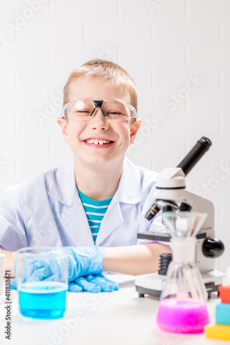 A schoolboy with a microscope examines chemicals in test tubes, conducts experiments - a portrait on a white background. Concept for the study of coronavirus in the laboratory © kosmos111