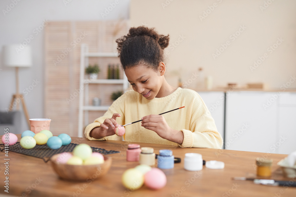 Minimal portrait of smiling African-American girl hand painting Easter eggs with pastel colors while enjoying DIY decorating at home, copy space - obrazy, fototapety, plakaty 