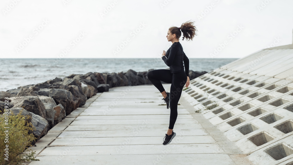 Outdoor workout concept. Fit slim woman with curly hair bounces up on an urban embankment with concrete slabs. Healthy lifestyle