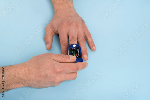 Human hand pulse oximeter used to measure pulse rate and oxygen levels with medical blue background with copy space. Male hand measures heart rate with heart rate monitor top view, Medical concept.