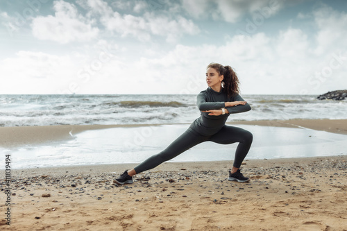 Curly sports woman in sportswear doing body warming up or stretching exercise on beach. Healthy lifestyle