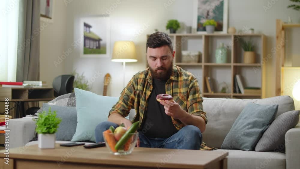 Young man makes a difficult choice between carrots and donuts Young man makes a difficult choice between carrots and donuts
