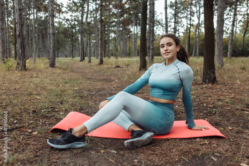 Young fitness woman sit on mat in the forest. Healthy lifestyle concept