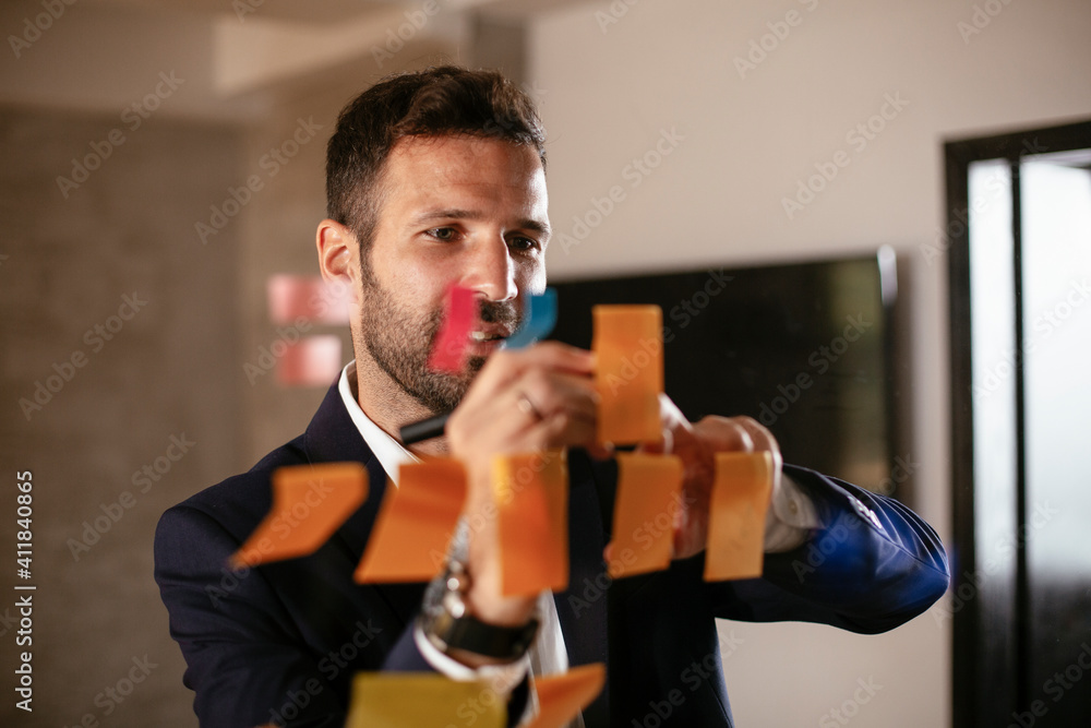 Businessman in conference room use sticky notes on glass wall. Handsome businessman making a business plan Businessman in conference room use sticky notes on glass wall. Handsome businessman making a business plan
