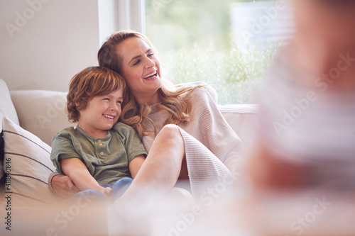 Mother Relaxing With Children On Sofa At Home Watching TV Together