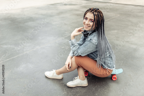 Extraordinary female millennial skater with colorful makeup, African braids in a skate park. Youth, lifestyle concept
