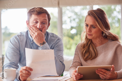 Worried Couple With Bills And Digital Tablet Sitting At Table At Home Reviewing Domestic Finances photo