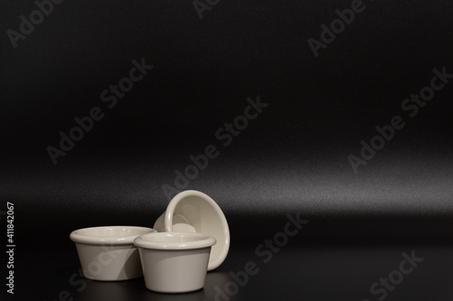 Three empty light colored containers on a black background with room for copy