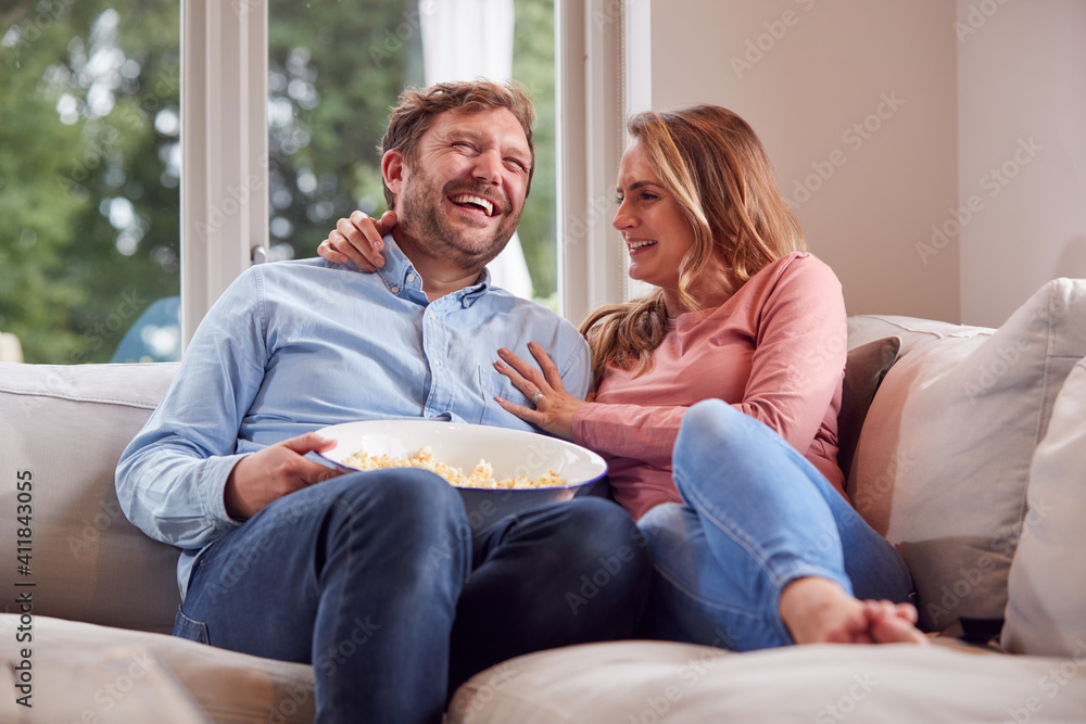 Obraz premium Couple On Date Night Sitting On Sofa At Home Laughing And Watching TV With Popcorn