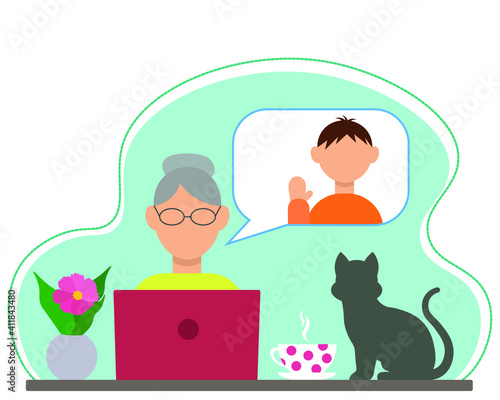 Grandmother sits at a table with a laptop, she communicates with her grandson on the Internet, on the table: a flower, a cup of tea and a cat