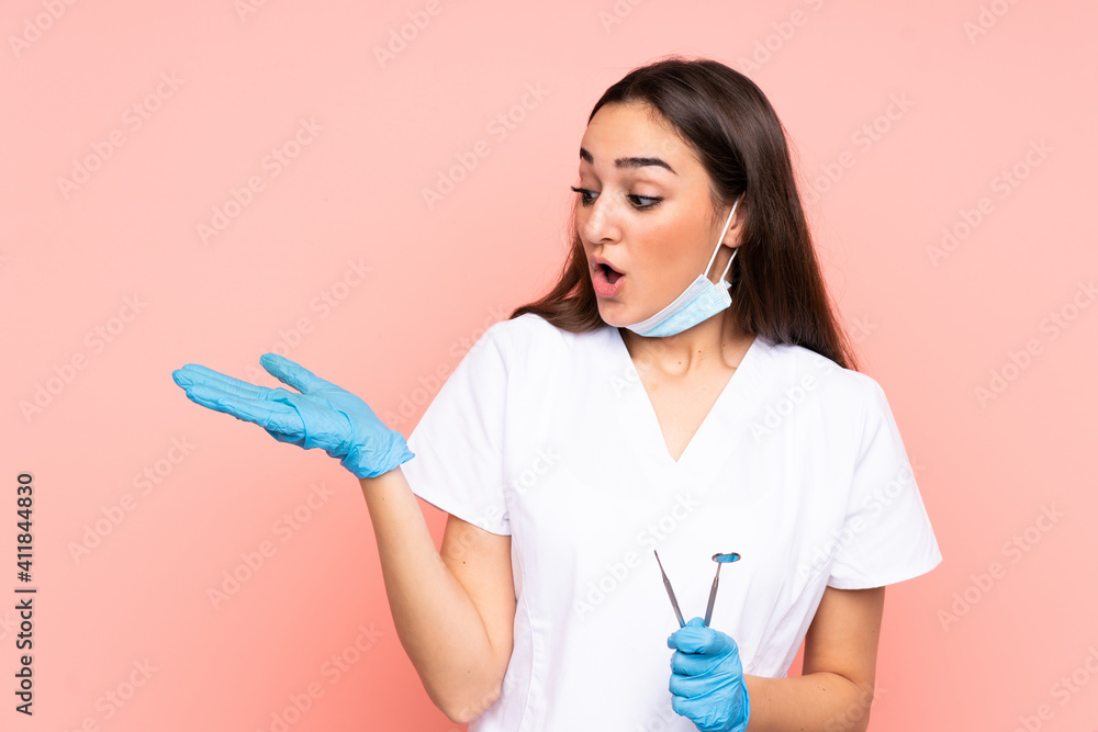 Woman dentist holding tools isolated on pink background holding copyspace imaginary on the palm Woman dentist holding tools isolated on pink background holding copyspace imaginary on the palm