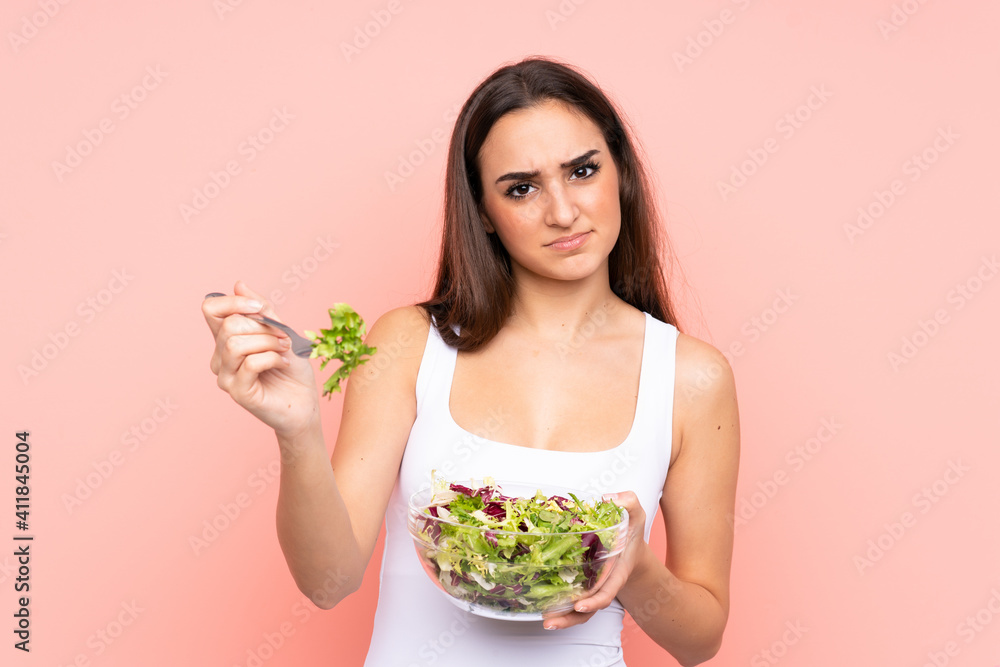 Young caucasian woman holding a salad isolated on pink background Young caucasian woman holding a salad isolated on pink background