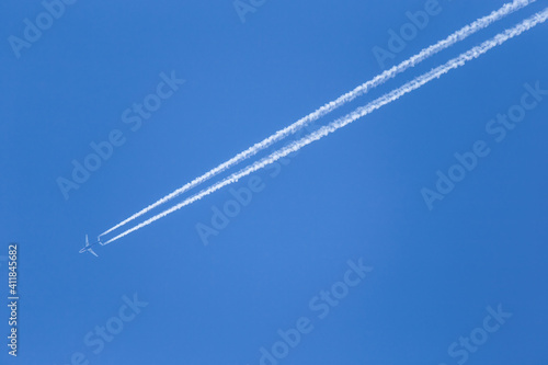 Airplane is flying high in the clear blue sky. Two white condensation trail cross air space.
