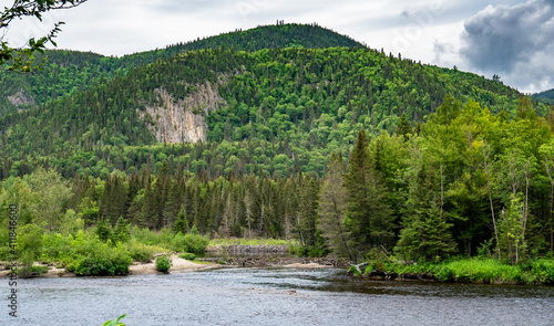 Huge cliffs with green trees everywhere on it facing two dams made by beavers near Fjords du Saguenay in Quebec Province, Canada