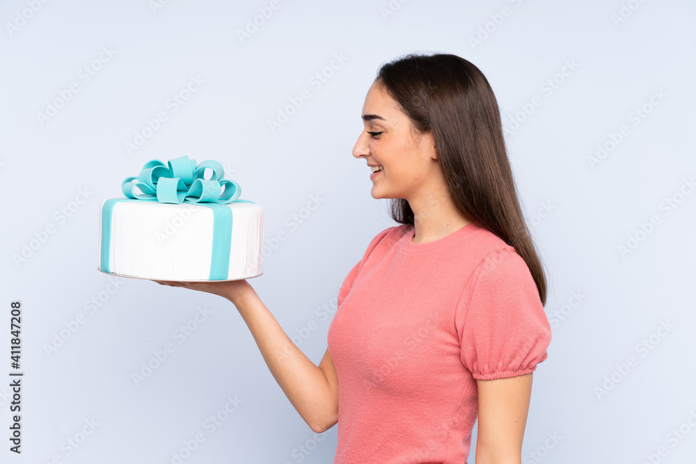 Pastry chef holding a big cake isolated on blue background with happy expression Pastry chef holding a big cake isolated on blue background with happy expression