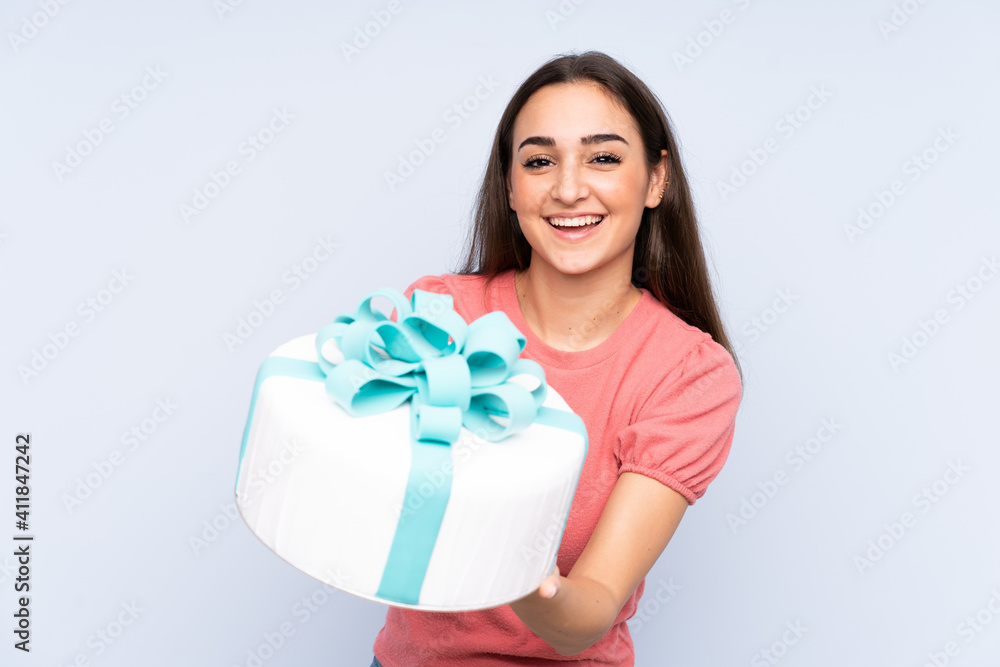 Pastry chef holding a big cake isolated on blue background Pastry chef holding a big cake isolated on blue background