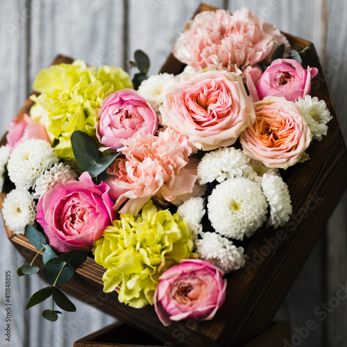 Wooden basket in the shape of a heart with pink roses and white, yellow flowers stands on a stand against a gray background