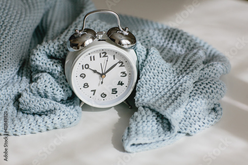Gray knitted plaid and alarm clock on a white background. Seasonal time change, daylight saving time concept.