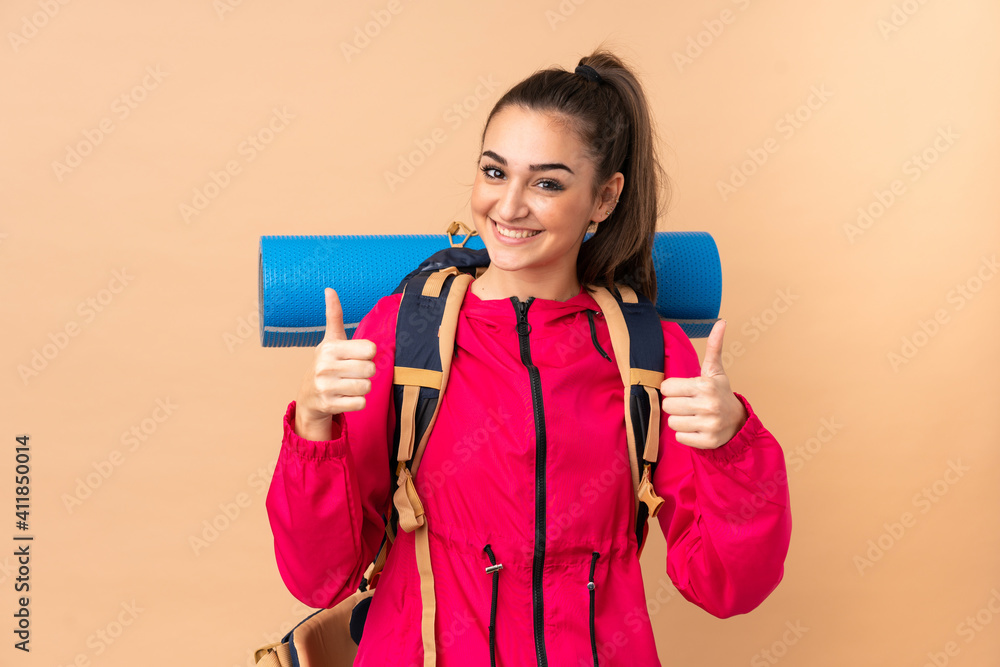 Young mountaineer girl with a big backpacker isolated on beige background giving a thumbs up gesture Young mountaineer girl with a big backpacker isolated on beige background giving a thumbs up gesture