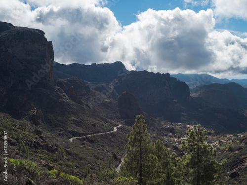 Scenic view of amazing landscape from path to Roque Nublo rock formation with winding road, mountains, green pine trees and blue sky, white clouds. Gran Canaria, Canary Islands, Spain