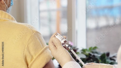 A doctor draws covid vaccine into a syringe to vaccinate an old woman. Senior woman gets a COVID-19 vaccine at home.