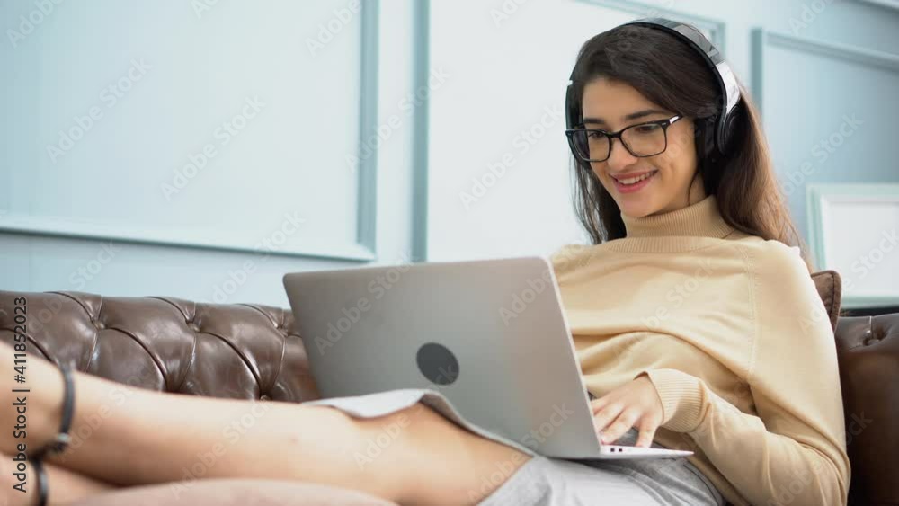 happy business woman working with laptop computer and listening music by headphone and sing a song sitting on sofa in office . young female learning online at home . happy business woman working with laptop computer and listening music by headphone and sing a song sitting on sofa in office . young female learning online at home .
