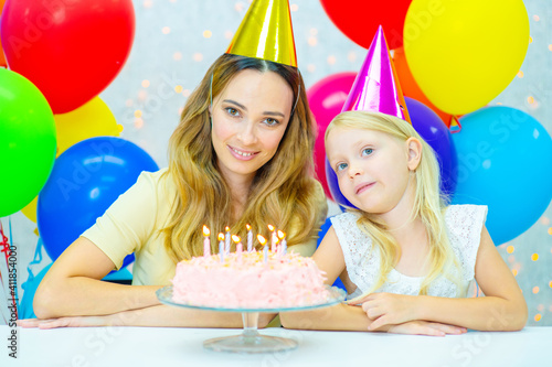 Mom with a smile and her daughter during the celebration of the birthday in festive caps and around the day of the birthday cake photo