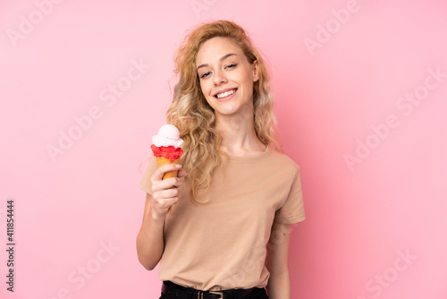Young blonde woman holding a cornet ice cream isolated on pink background smiling a lot