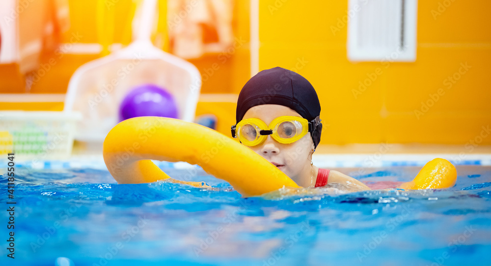 Little kid girl with glasses learning to swim with pool noodle