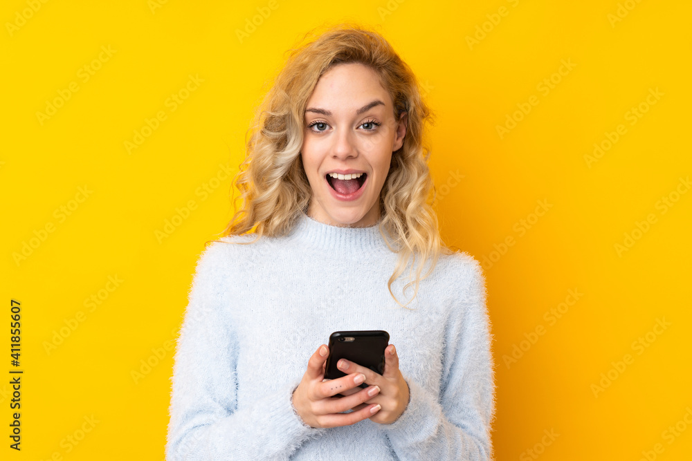 Young blonde woman isolated on yellow background surprised and sending a message Young blonde woman isolated on yellow background surprised and sending a message
