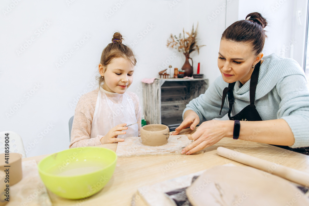 Mother and daughter decorate a clay plate before firing in a pottery studio, decorate a plate with lavender branches Mother and daughter decorate a clay plate before firing in a pottery studio, decorate a plate with lavender branches
