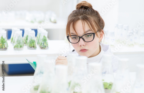 A worker in a biological laboratory fills out a report by examining plants grown in a nutrient solution in flasks. Biological research at the university