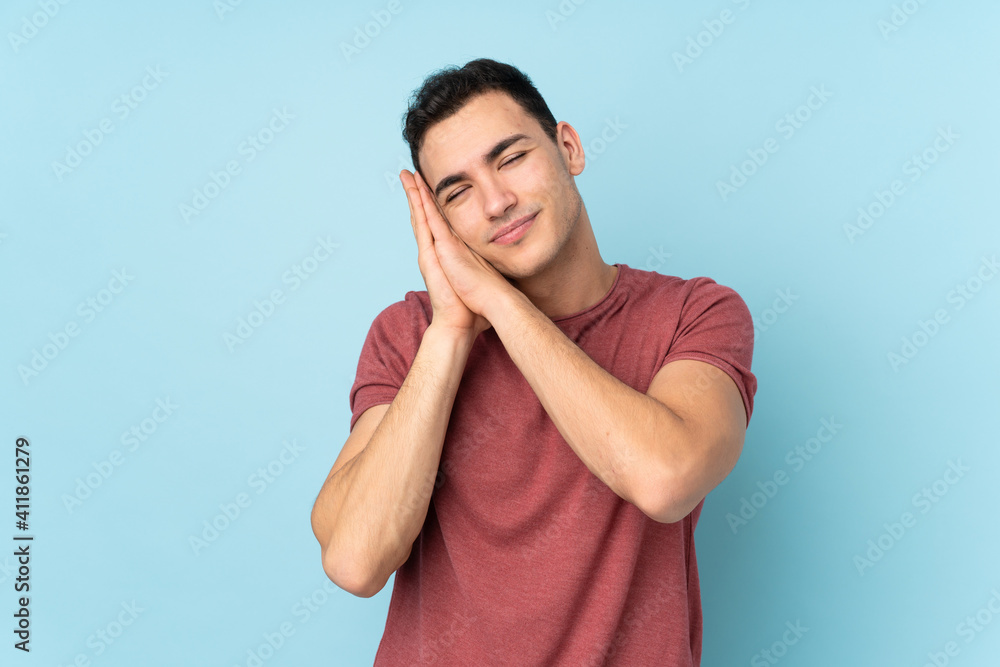 Young caucasian handsome man isolated on blue background making sleep gesture in dorable expression Young caucasian handsome man isolated on blue background making sleep gesture in dorable expression